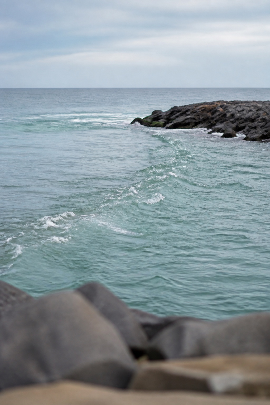Tide rip forming off the end of a stone jetty, with a clear seam of broken water where a current plug would be swung through